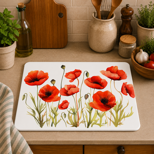 A rectangular glass cutting board with a vibrant red poppy floral design, displayed on a beige kitchen countertop surrounded by kitchen items like a wooden cutting board, cutting board, a pepper mill, and a striped cloth.